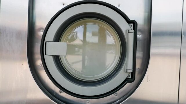 Machines &agrave; laver &ndash; Gros plan sur porte d'une machine &agrave; laver industrielle dans une laverie automatique publique avec une couette qui tourne dedans.