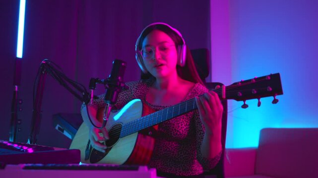 Social media sharing concept. Asian woman musician live streaming online guitar class with smartphone. Female guitarist making video lessons and tutorials for internet vlog website classes.