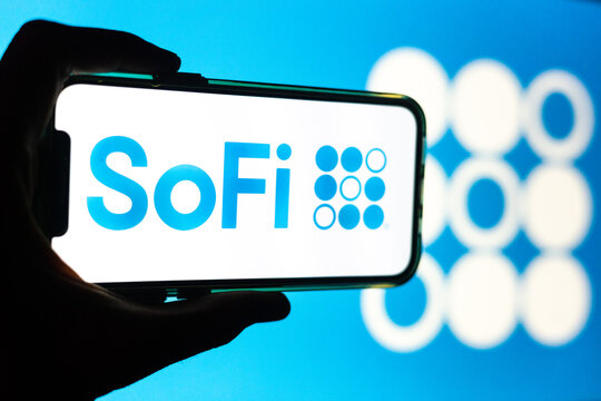 Silhouette of Hand Holding iPhone with SoFi Logo in Front of Computer Screen Displaying Logo &ndash; Personal Finance and Online Banking Solutions (SOFI)
