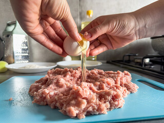 Woman prepare dinner breaks an egg into a fresh minced meat at home
