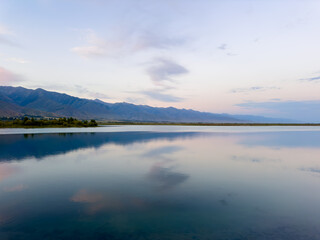 Fototapeta premium Quiet mountain lake, evening light on the water, Kyrgyzstan. Still water and mountain reflection in the lake