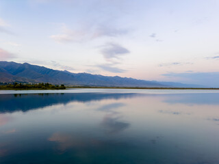 Fototapeta premium Quiet mountain lake, evening light on the water, Kyrgyzstan. Still water and mountain reflection in the lake