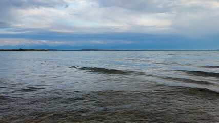 Fototapeta premium The calm waters of Issyk-Kul lake reflect dramatic clouds and mountains. Silence and tranquility in a natural oasis in Kyrgyzstan