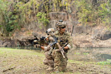 Two of militaries or soldiers stay in battlefield near the river with holding gun also look to different direction during outdoor practice.