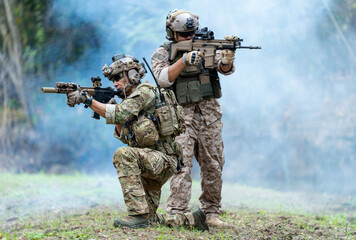 Militaries or soldiers stay in battlefield near the river with one sit down and one stand and point gun forward direction during outdoor practice.