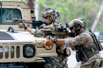 Two militaries or soldiers stay in front of humvee car area of car hood and point gun to left side...