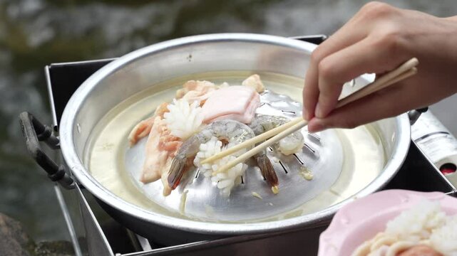 chopsticks picking up a piece of sliced pork and beef on the pan .Thai BBQ Mookata.