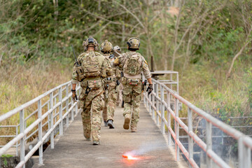 Back of military or soldier team with battle suit walk on the bridge near flare firework during...