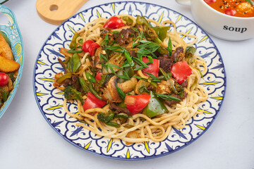 Closeup on uyghur laghman noodles in a traditional plate on the dark wooden table, horizontal