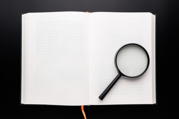 A magnifying glass placed on the empty page of the opened book on black background