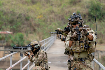 Fototapeta premium Close up military or soldier team with battle suit stand on the bridge and point gun to enemy in different direction during outdoor practice.