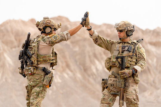 Two of soilders or militaries with war suit and gun touch hands together during outdoor practice.
