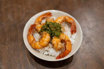 Stir-fried shrimp served over white rice in a bowl on a wooden table.