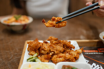 Chopsticks lifting a piece of deep-fried chicken.