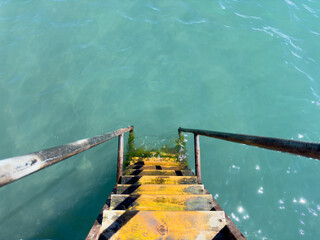 Yellow wooden steps with metal handrails descend into clear turquoise water. Top view creating an...