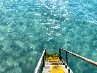 Yellow wooden steps with metal handrails descend into clear turquoise water. Top view creating an...