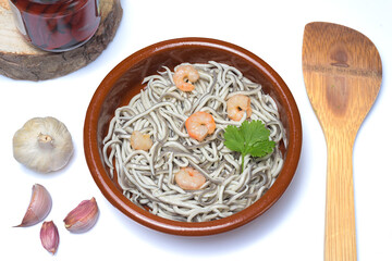 Eels with garlic prawns in a clay pot with garlic cloves, a coriander leaf, vegetables and wooden spoon on a white background