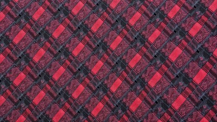 Fabric with a chequered pattern with an alternation of discreet red and dark shades. The texture creates a sense of relief and warmth, giving the material a cosy and classic look