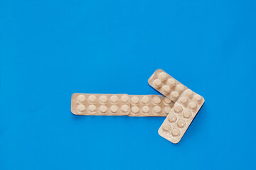 An arrow made of blister packs of white tablets against a blue background, close-up, medical backdrop, direction of treatment.