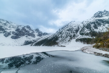 Obraz premium tranquil view of Morskie Oko in Tatra National Park, Poland, showcasing majestic snow-covered mountains, serene frozen lake, and reflections on a chilly winter day. Winter landscape
