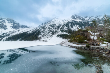 Obraz premium tranquil view of Morskie Oko in Tatra National Park, Poland, showcasing majestic snow-covered mountains, serene frozen lake, and reflections on a chilly winter day. Winter landscape