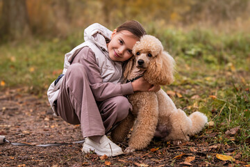 Adorable little girl hugging her poodle dog on walk in autumn park.