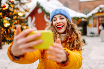 Happy woman wear winter season clothes taking selfie xmas market urban city street. Christmas, new...