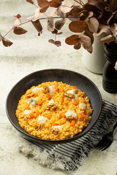 Vertical image of lunch with homemade Pumpkin Risotto with Gorgonzola Cheese and walnuts. Vase with autumn gried leaves. Italian meal.