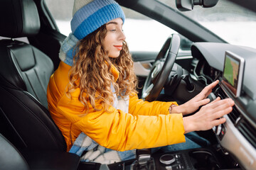 Naklejka premium Young woman holds her hands over the car's hot air outlet. Cold hands. Travelling in winter.