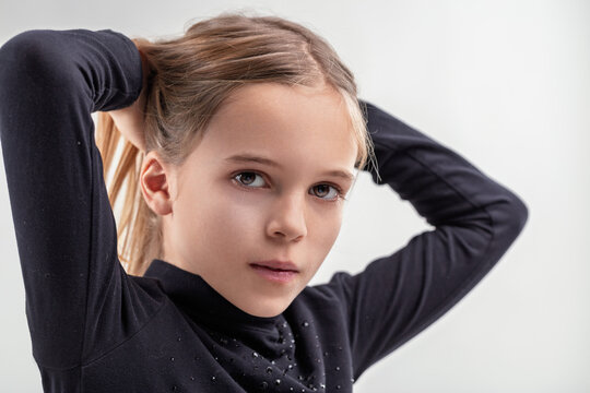 Young girl adjusting hair with thoughtful expression on white ba