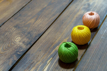 Multicolored balls of thread lie on a wooden table. The concept of making handmade knitted...
