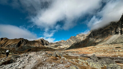 Low clouds hover around the mountain peaks, partially obscuring them and creating a misty atmosphere with a hiker in the left 