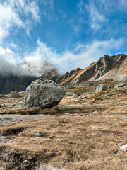 Foggy High Tatras with a large boulder in the foreground, surrounded by dry grass and rocky terrain 