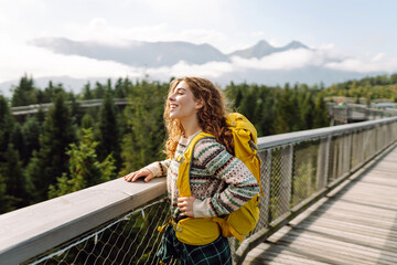 Traveler woman enjoys nature as she stands on a wooden bridge overlooking mountains. Tourism and...