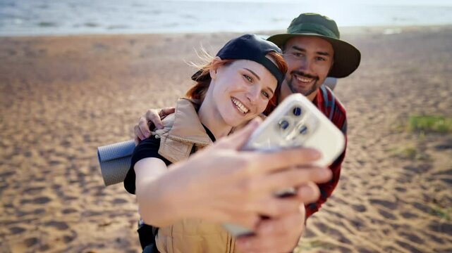 Happy woman taking selfie with her boyfriend while they traveling in nature. Tourism and travel in beautiful natural landscapes, smiling lady looking to frontal camera of her smartphone, good mood