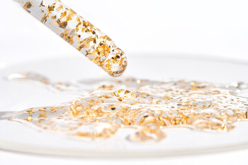 Luxurious golden serum with gold flakes in dropper on a glass surface for skincare and beauty