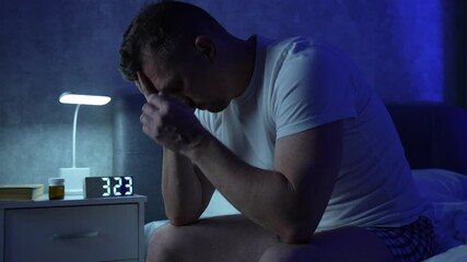 Man sitting on bed suffering from insomnia. Depressed and tired man in bed with migraine or headache. Health problem, insomnia or panic attack