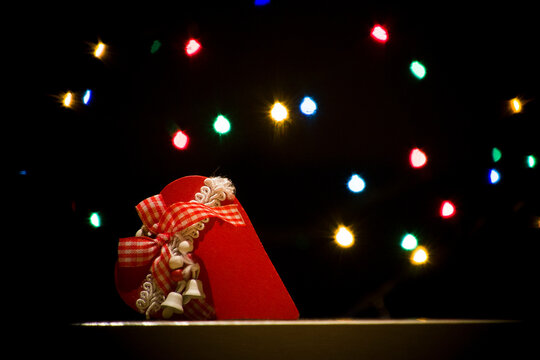 Red Christmas wooden heart with white bells. Colorful background lights, on a black background, with bokeh effect. Christmas postcard.