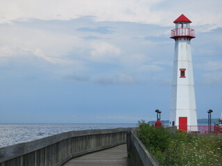 Tall White St Ignace Michigan Lighthouse with Red Roof Window and Door Down Boardwalk on Coast of Lake Huron under Beautiful Clouds and Sky