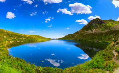 Panoramic view of a mountain lake. The blue sky with clouds reflecting on the mirrored lake water