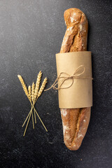 A rustic loaf of bread with unique textures sits alongside wheat stalks, placed creatively on a dark background, ideal for concepts of food artistry or rustic lifestyles.