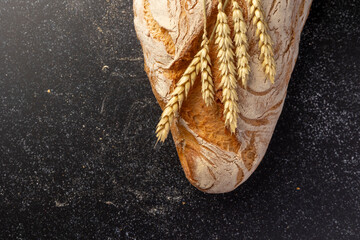 A rustic loaf of bread with unique textures sits alongside wheat stalks, placed creatively on a...