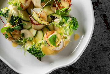 A gourmet dish featuring seared scallops, sliced cucumbers, radish, green garnishes, and a drizzle of sauce on an elegant white plate. Perfectly plated for a fine dining experience