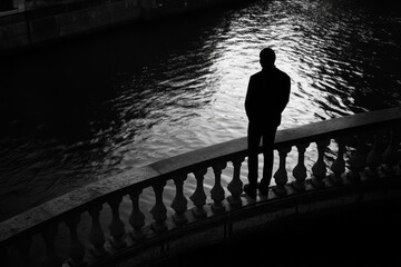 Fototapeta premium Silhouette of a man standing by a curved riverbank with reflective water surface