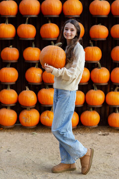 brunette girl holding a pumpkin in front of a wall of pumpkins