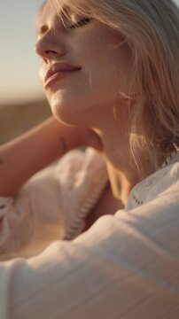 A young blonde woman with closed eyes is bathed in the golden light of sunset. Her serene face embodies peace and tranquility, ideal for themes of relaxation, nature, and beauty.
