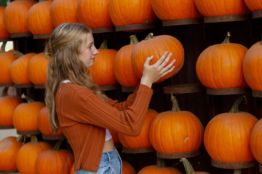 beautiful blond teenage girl picking a pumpkin from a wall of pumpkins
