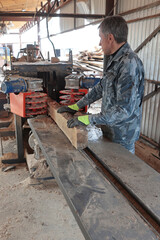 A worker saws a tree trunk on a machine. The sawmill. The process of processing logs at a sawmill. The concept of production. Vertical photo.