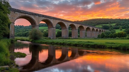 A stone viaduct spans a river with a dramatic sunset sky reflecting in the water.