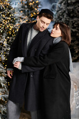 A loving couple enjoys a festive moment surrounded by snow and twinkling lights, embracing the holiday spirit.